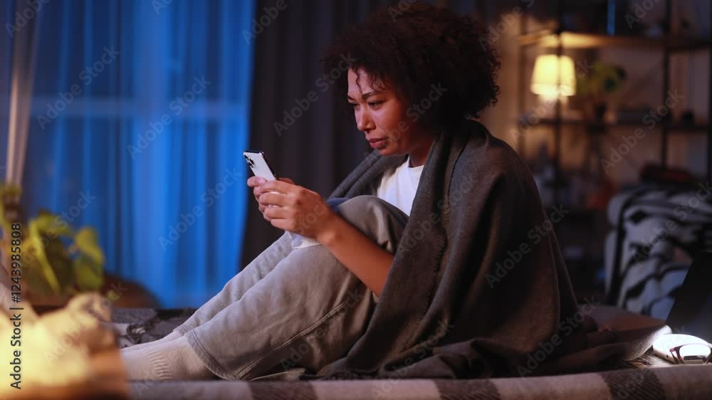 Crying young african american woman with smartphone under the blanket and reading bad news email break up message from ex-boyfriend or personal problems at home at late night Crying young african american woman with smartphone under the blanket and reading bad news email break up message from ex-boyfriend or personal problems at home at late night
