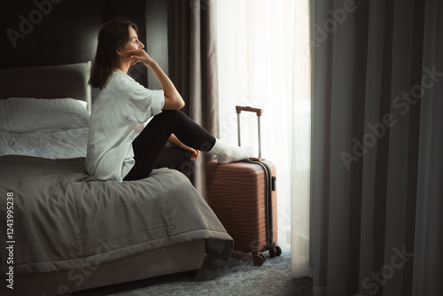 Depressed lonely woman sitting in hotel room with her suitcase nearby. Female emotional crisis during solo travel, feeling sense of loneliness, escape from complicated situation, or violence 