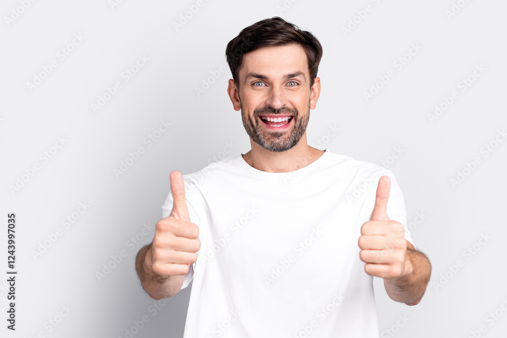Smiling Young Man Showing Thumbs-Up Gesture in a White T-Shirt Against a Light Grey Background Smiling Young Man Showing Thumbs-Up Gesture in a White T-Shirt Against a Light Grey Background