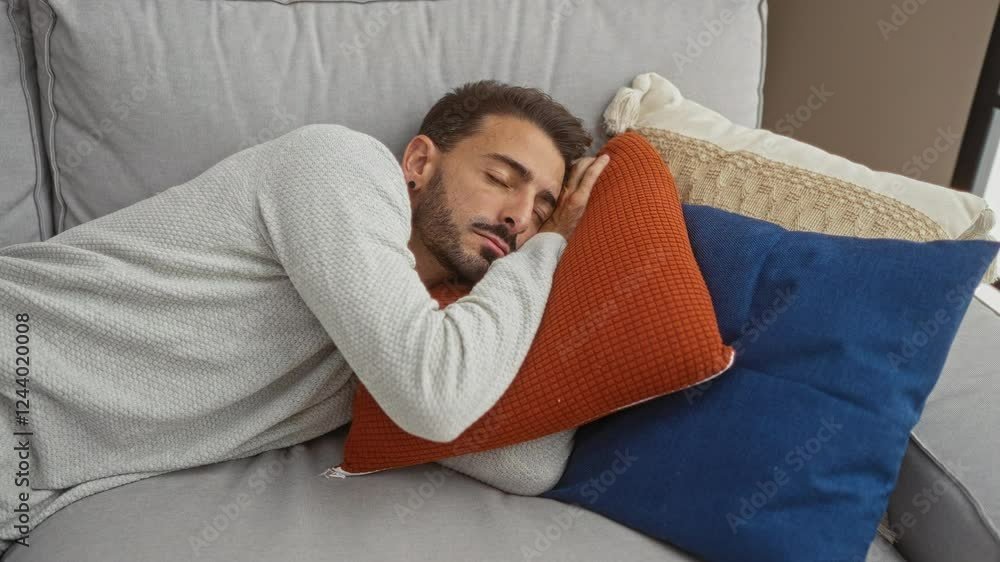 Young man relaxing indoors lying on a couch with colorful pillows in a cozy living room setting. Young man relaxing indoors lying on a couch with colorful pillows in a cozy living room setting.