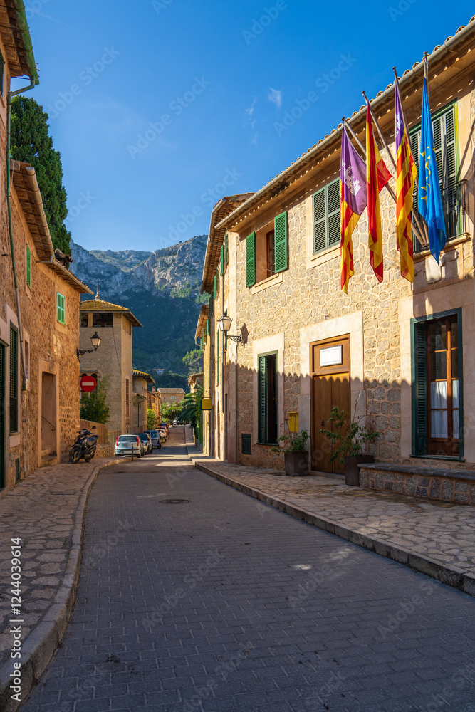 Fototapeta premium Narrow street in village Deia, Mallorca, lined with rustic stone houses. Window decorated with many colorful flags . Balearic Islands, Spain