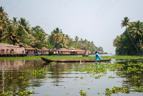 Tableau sur toile A woman paddling a small wooden boat along the backwaters of Kerala, India