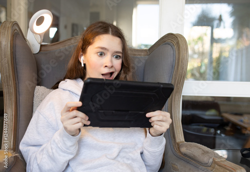 Teenage girl sitting at home on an armchair with iPad