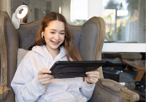 Teenage girl sitting at home on an armchair with iPad