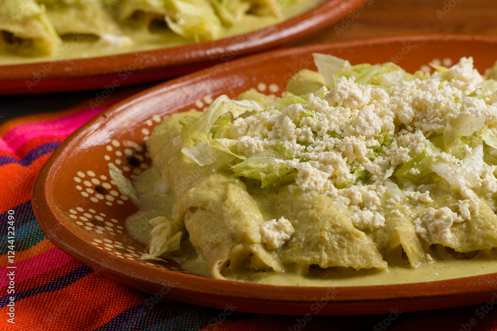 Green enchiladas with lettuce and cheese served in a clay dish. Colorful tablecloth. Close up. Green enchiladas with lettuce and cheese served in a clay dish. Colorful tablecloth. Close up.