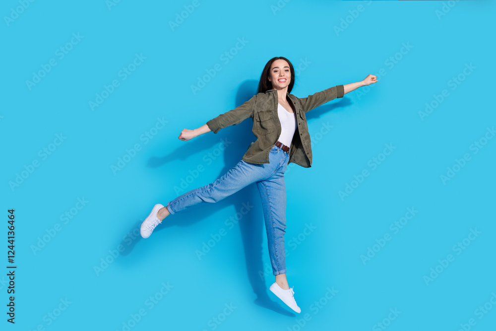 Fototapeta premium Young woman jumping joyfully against a vibrant blue background, exuding happiness and positive energy in casual trendy attire