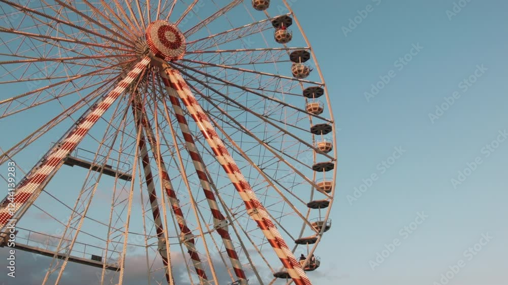 Ferris wheel from below during golden hour, with warm sunlight illuminating the intricate gondola designs. The clear blue sky serves as a backdrop, highlighting the s Ferris wheel from below during golden hour, with warm sunlight illuminating the intricate gondola designs. The clear blue sky serves as a backdrop, highlighting the s