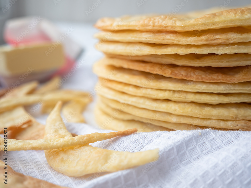 A pile of baked thin round buttery layers, dough scraps and butter on a white waffle towel ready to make a shortcrust puff pastry Napoleon cake.