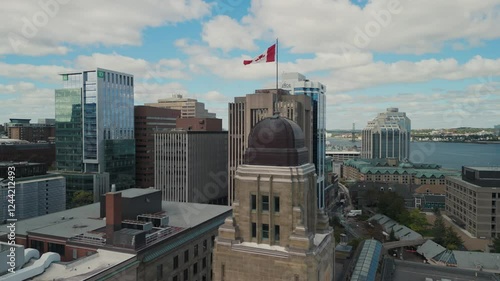 Aerial View Of An Ancient Skyscraper With A Waving Flag On The Tower At Sunset In Halifax. Modern Skyscrapers Frame The Scene, Highlighting The Contrast Between Old And New Architecture.