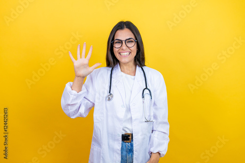 Young brunette doctor woman wearing stethoscope standing over isolated yellow background showing and pointing up with fingers number five while smiling confident and happy