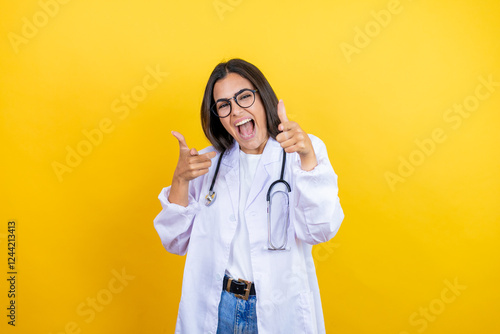 Young brunette doctor woman wearing stethoscope standing over isolated yellow background pointing to you and the camera with fingers, smiling positive and cheerful