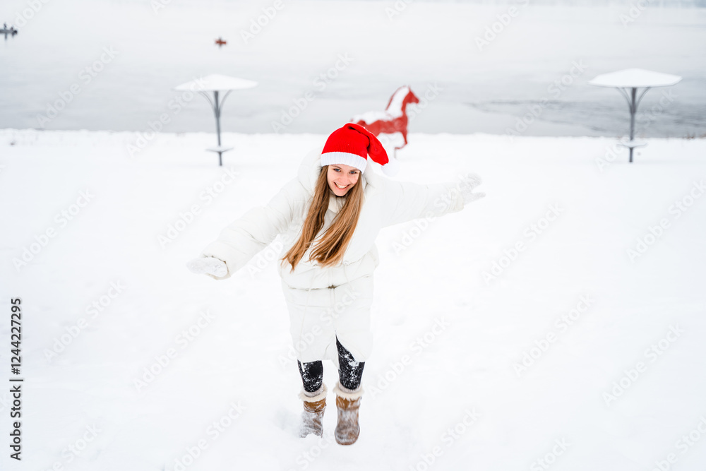Obraz premium Portrait of a beautiful young woman in a winter red hat smiling and playing with snow, picturesque winter forest