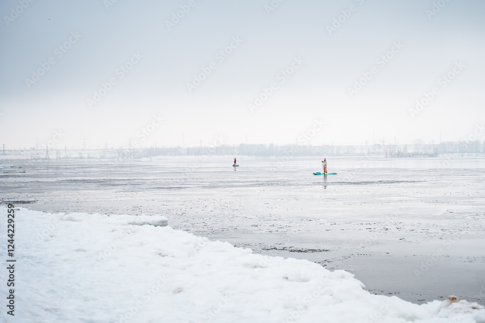 Fishermen in boats on the Volga River catch fish in winter. People on the Sup Board. Winter fishing. Beautiful gloomy foggy landscape with mountains and ice on the river. Fishermen in boats on the Volga River catch fish in winter. People on the Sup Board. Winter fishing. Beautiful gloomy foggy landscape with mountains and ice on the river.
