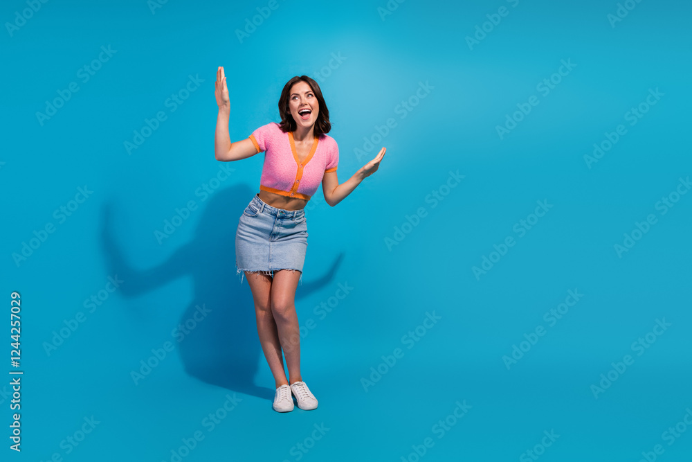 Obraz premium Energetic young woman posing in casual summer outfit against bright blue background, expressing joy with a lively attitude.