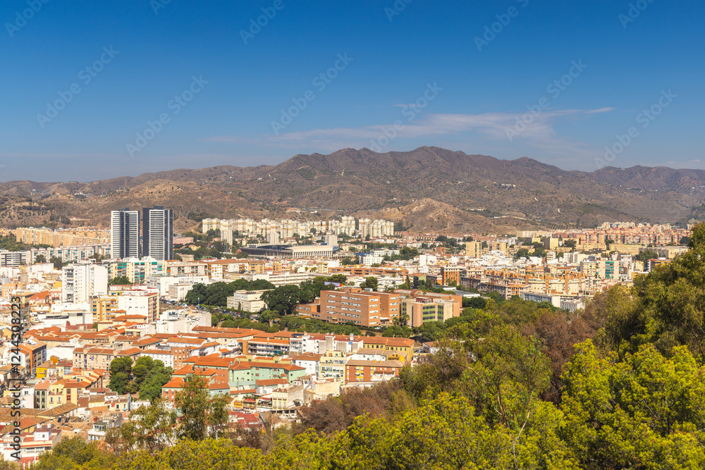 Obraz premium Malaga, seaside city in Andalusia, Spain, Europe. Panoramic view of a city nestled against mountains under a clear blue sky. Buildings, trees, and hills create a picturesque landscape.