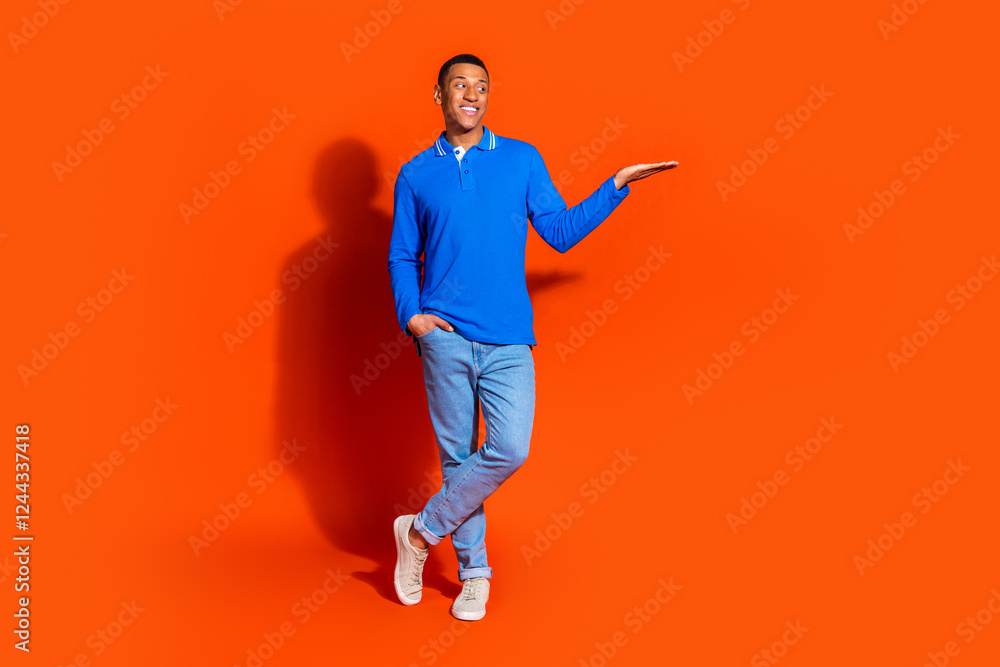 Young man in blue polo shirt posing against a vibrant orange background Young man in blue polo shirt posing against a vibrant orange background