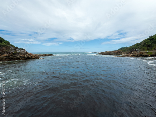 Tsitsikamma National Park, South Africa. wavy ocean, suspension foot bridge, blue cloudy sky