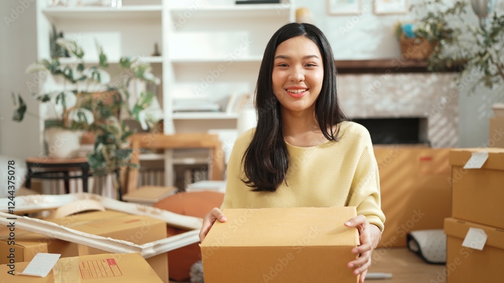Young female business owner holding cardboard while standing at shop. Attractive happy entrepreneur carrying package and box while preparing for delivery or shipping process at home office. Myrmidon. Young female business owner holding cardboard while standing at shop. Attractive happy entrepreneur carrying package and box while preparing for delivery or shipping process at home office. Myrmidon.