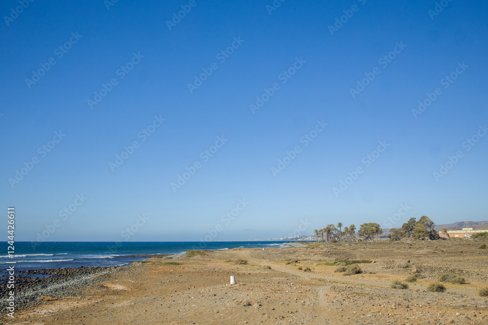Wide, open beach in Gran Canaria with clear blue sky. Mix of sand and pebbles on the shore.