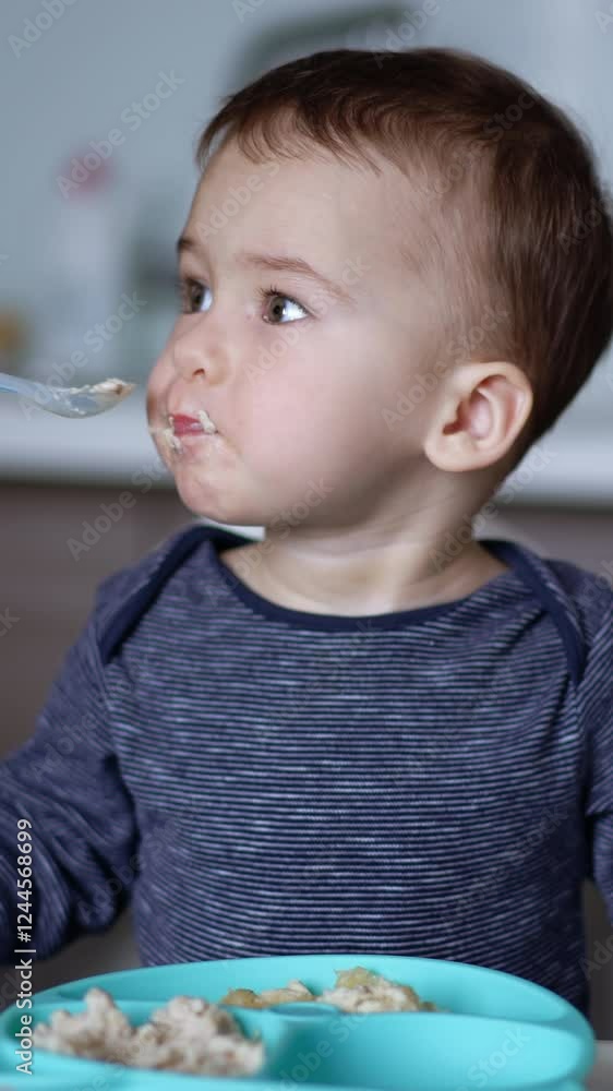 Mealtime for a cute Caucasian toddler. Baby sits at high chair with fork in hand while mom feeds him from spoon. Mealtime for a cute Caucasian toddler. Baby sits at high chair with fork in hand while mom feeds him from spoon.