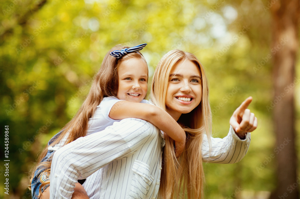 Fototapeta premium Look There. Mother Carrying Daughter Piggyback And Pointing Finger Spending Time Walking Together In Park Outdoor On Weekend