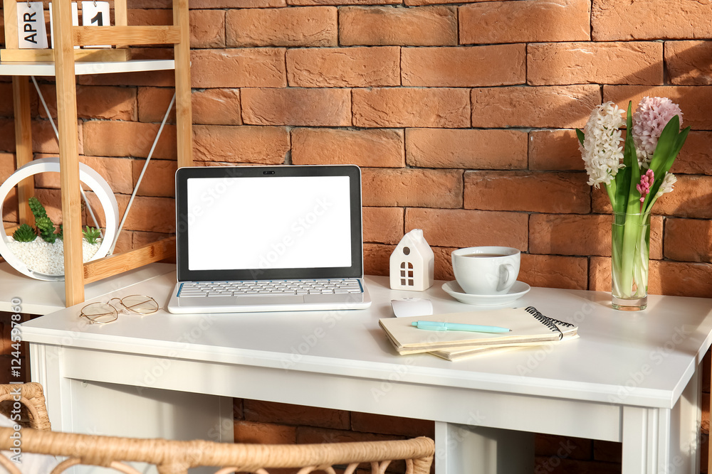 Comfortable workplace with modern laptop and hyacinth flowers near brown brick wall Comfortable workplace with modern laptop and hyacinth flowers near brown brick wall