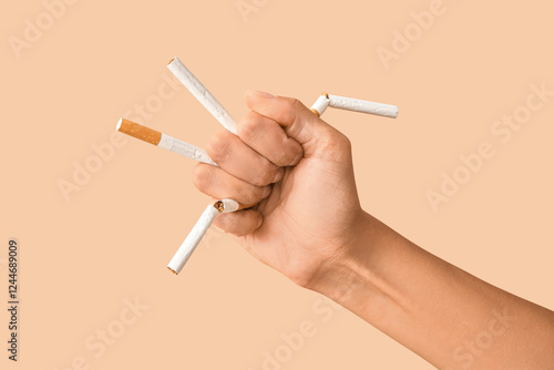 Female fist with broken cigarettes on beige background. Stop smoking concept photo