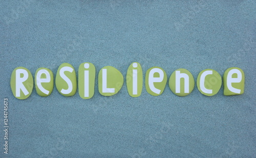 Resilience, the capacity to withstand or to recover quickly from difficulties, word composed with green colored hand painted stone letters over green sand