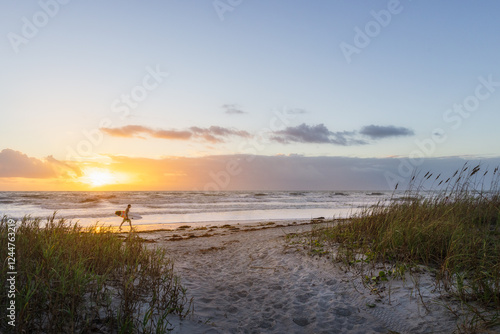 Surfer walking along beach at sunrise in Cocoa Beach, Florida