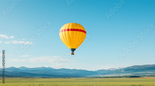 Yellow Hot Air Balloon over Mountains: A vibrant yellow hot air balloon with a red stripe drifts serenely against a clear blue sky, with majestic mountains and a verdant valley stretching out below. photo