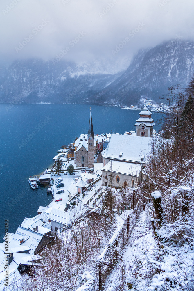 Hallstatt, Austria. Idyllic Alpine village snow-covered, serene lake, majestic mountains shrouded in a winter blizzard.