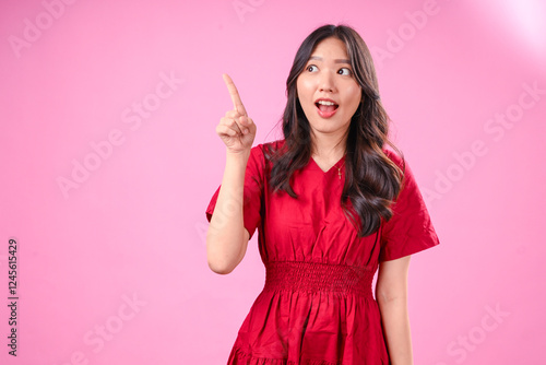 Фотография A young Asian woman with long wavy black hair wears a red dress, against a pink background