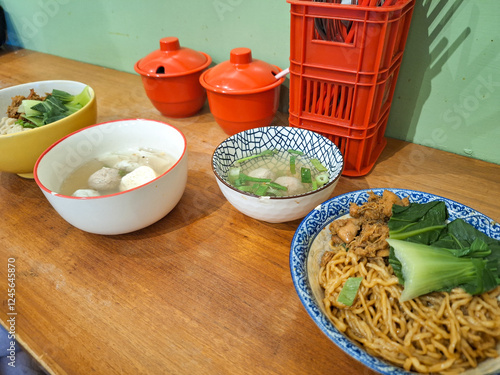 A bowl of yamin manis served with a bowl of meatballs soup on wooden table photo