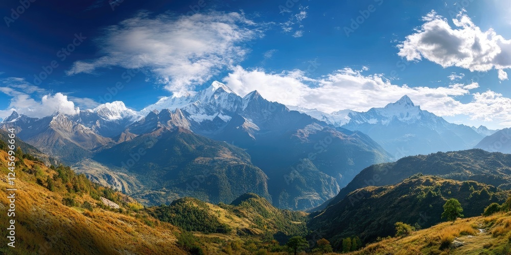 Obraz premium Majestic panoramic view of snow-capped mountains under a vibrant blue sky with wispy clouds and green hills in the foreground showcasing natural beauty.
