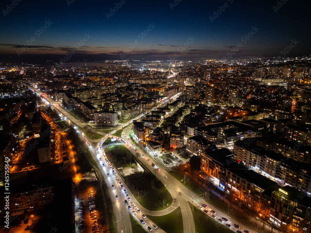 Fototapeta premium Aerial view of Varna, Bulgaria, at sunset, showcasing a vibrant cityscape with illuminated streets, moving traffic, and a glowing skyline. The coastal metropolis reflects urban energy and modern