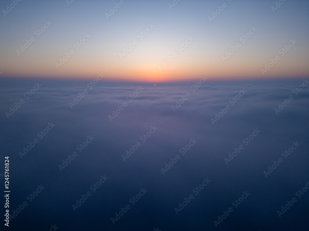 Fototapeta premium Aerial drone view above clouds at sunrise, high-altitude misty landscape with rolling fog and golden horizon, breathtaking cinematic aerial footage capturing the tranquil beauty of sky and clouds in