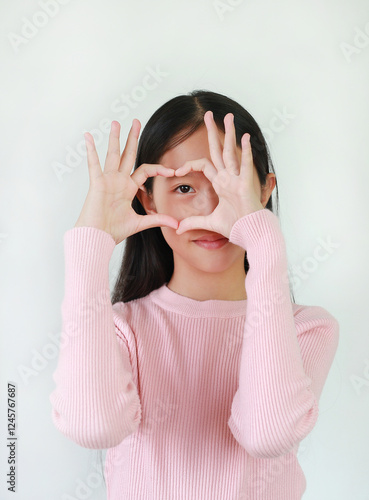 Asian girl preteen making heart figure or love sign by fingers at his eye on white.