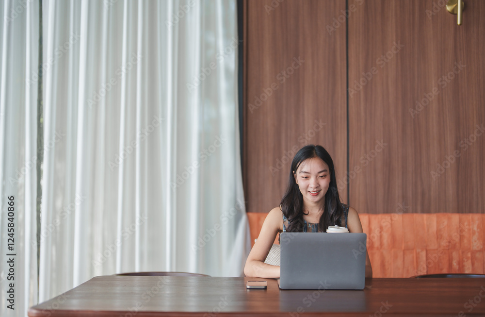 Young asian freelancer is smiling while working on her laptop in a modern office, enjoying a productive workday in a comfortable and stylish workspace Young asian freelancer is smiling while working on her laptop in a modern office, enjoying a productive workday in a comfortable and stylish workspace