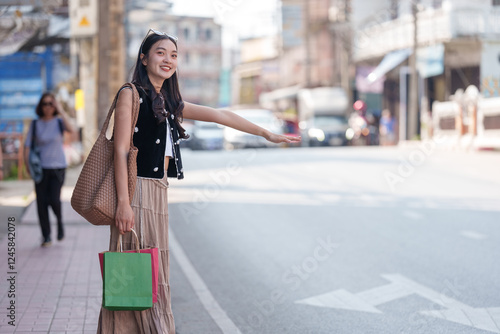 Happy shopper hailing a taxi cab after a successful shopping spree, holding colorful shopping bags and gesturing for a ride on a city street photo