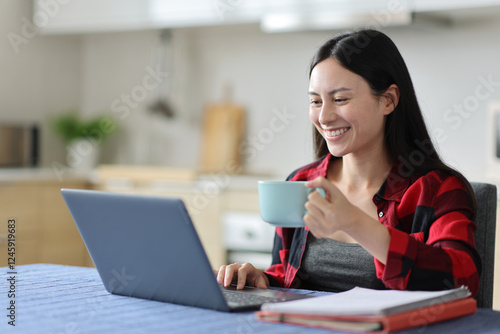 Happy asian woman drinking and e-learning using laptop photo