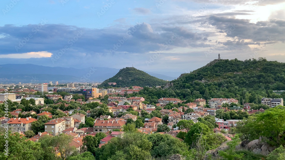 Obraz premium Scenic view of Plovdiv, Bulgaria, featuring the Alyosha monument, cityscape, lush hills, and cloudy sky. Take at Golden Hour.