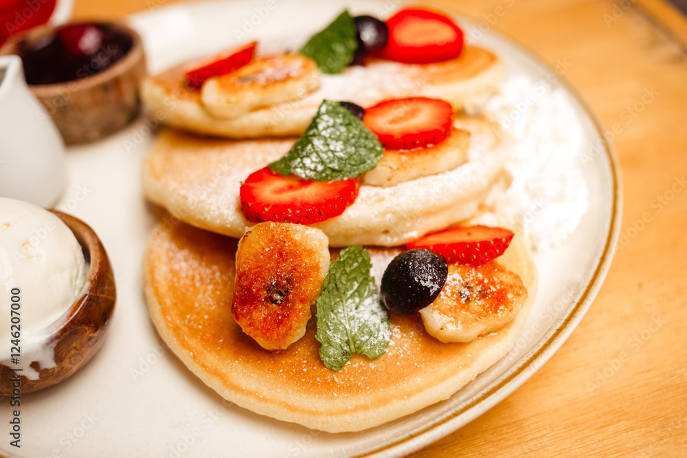 Pancakes with strawberries, fried bananas, ice cream and syrup on a wooden table. Delicious breakfast with fruits and berries Pancakes with strawberries, fried bananas, ice cream and syrup on a wooden table. Delicious breakfast with fruits and berries