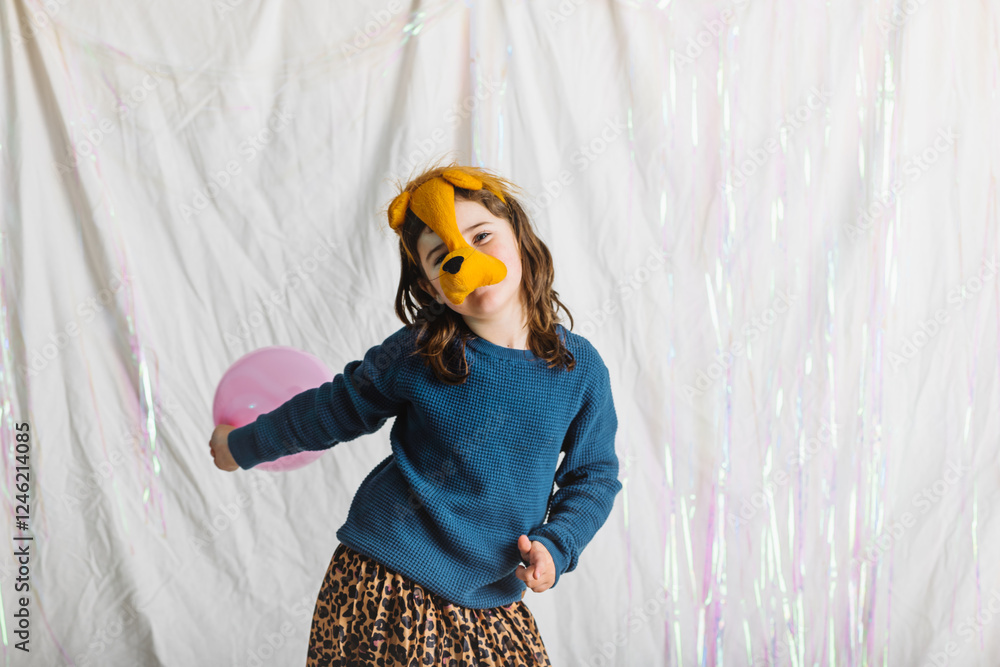 Obraz premium Elementary kid plays joyfully with a pink balloon wearing a fun lion headband in a colorful indoor setting
