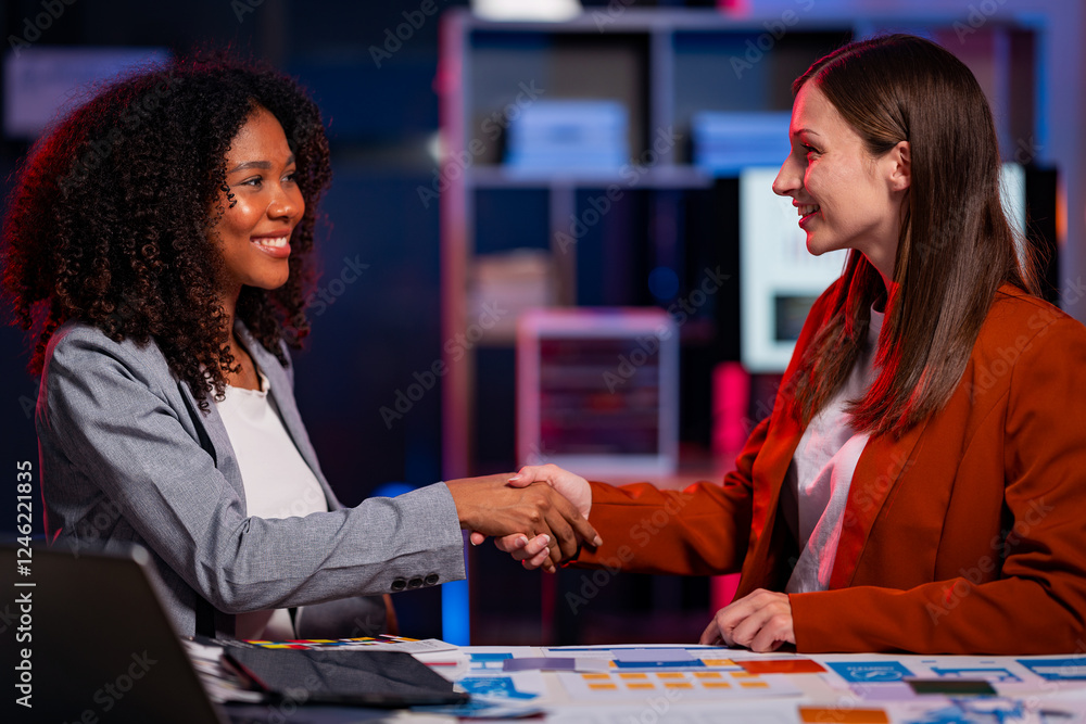 Fototapeta premium Two young businesswomen holding hands at the table making a deal in a business collaboration with an African woman