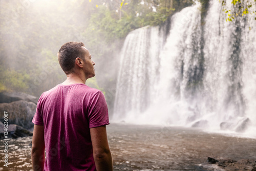 Man in front of high waterfall in mountains in tropical landscape. Travler in Camobodia.. photo