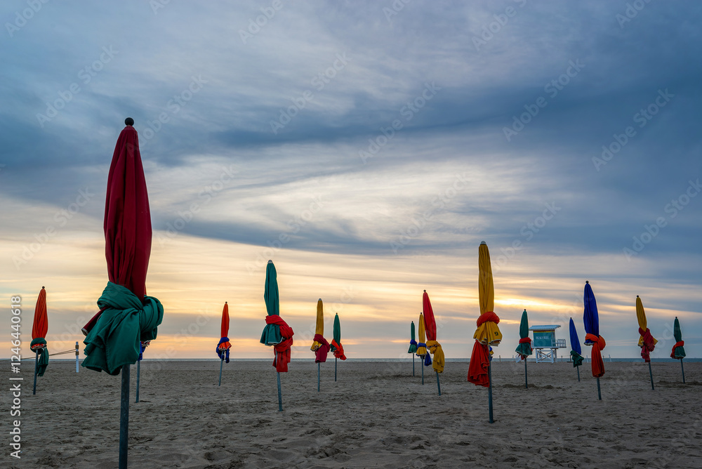 Beach of Deauville at sunset, famous vintage parasols and lifeguard station tower, in Normandy, France