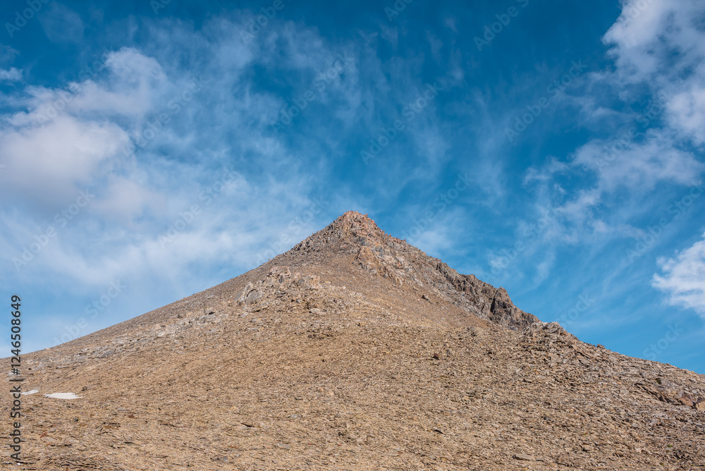 Sunlit pointy peak under clouds in blue sky. Triangle shaped stony pointy mountain top in bright sun. Pointed pile of stones of pyramid shape in changeable weather. Sharp rocky pinnacle in sunny day. Sunlit pointy peak under clouds in blue sky. Triangle shaped stony pointy mountain top in bright sun. Pointed pile of stones of pyramid shape in changeable weather. Sharp rocky pinnacle in sunny day.