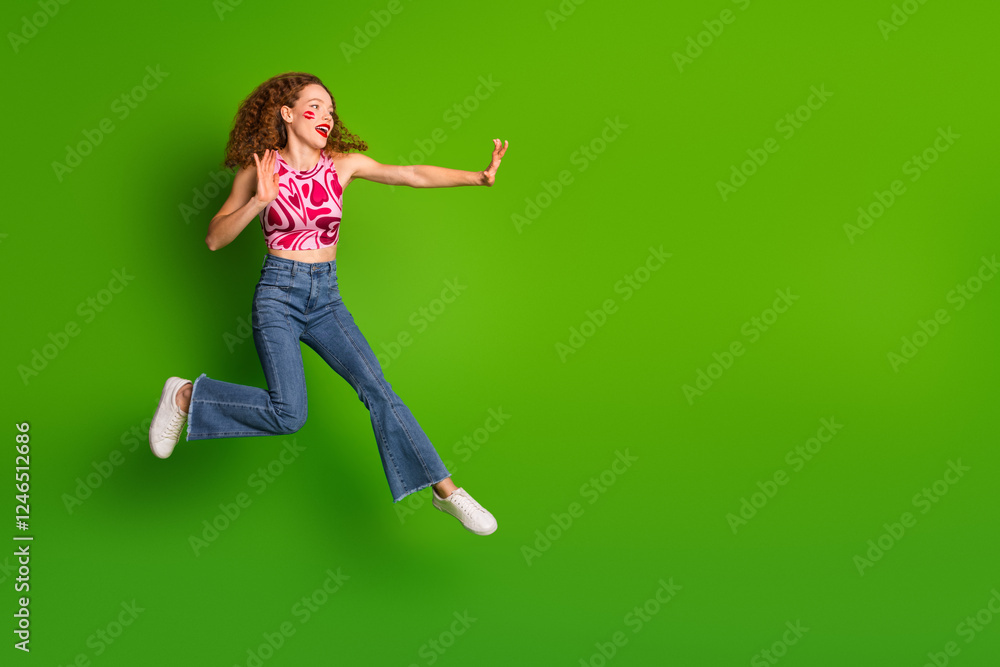 Energetic woman with red hair in stylish casual clothes jumping against a vibrant green background Energetic woman with red hair in stylish casual clothes jumping against a vibrant green background
