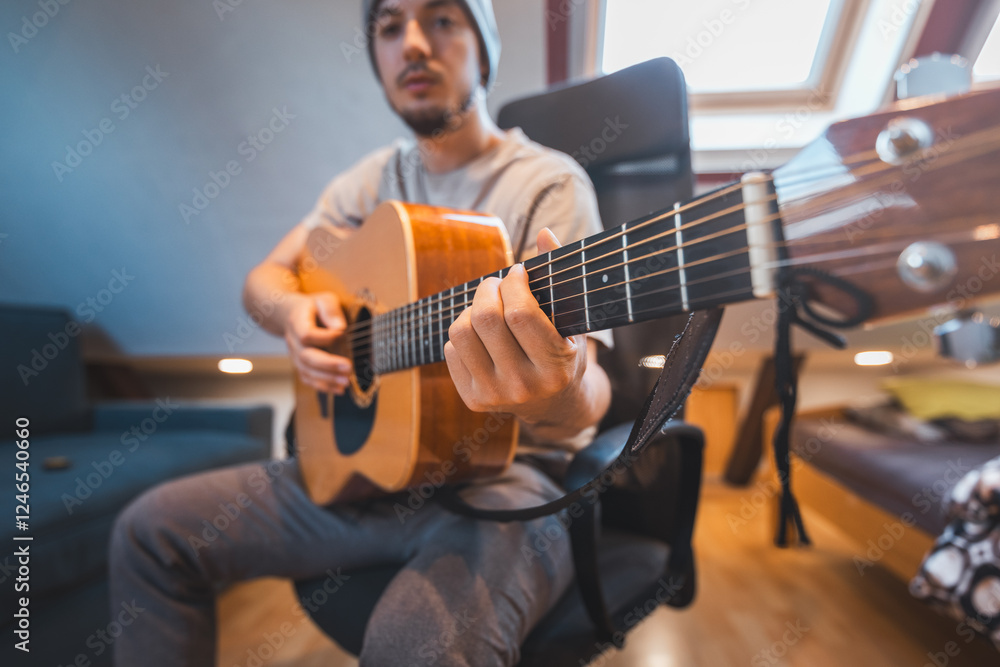 Obraz premium Man alone in the middle of a sunlit room enjoys playing a beautiful wooden acoustic guitar and composing new songs. Immersed in the sweet tones of the guitar. Music that heals the soul