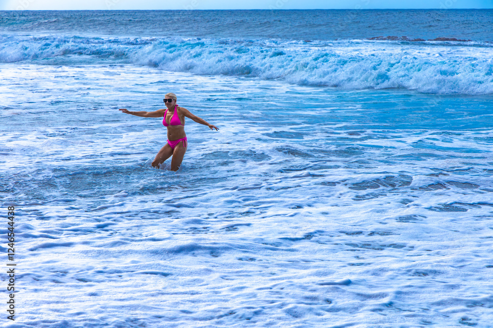 Young graceful woman in a pink swimsuit bathes in the Atlantic Ocean during high and dangerous waves Young graceful woman in a pink swimsuit bathes in the Atlantic Ocean during high and dangerous waves